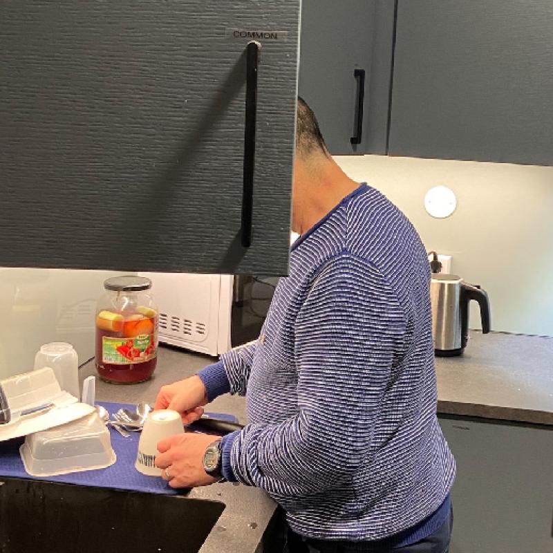 A man washes dishes, his face hidden by an open cupboard door