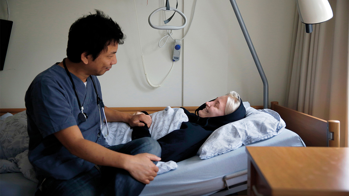 A man in medical uniform speaks to a patient in a hospital bed