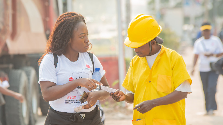 A woman in a Salvation Army t-shirt hands a flyer to a man on the street