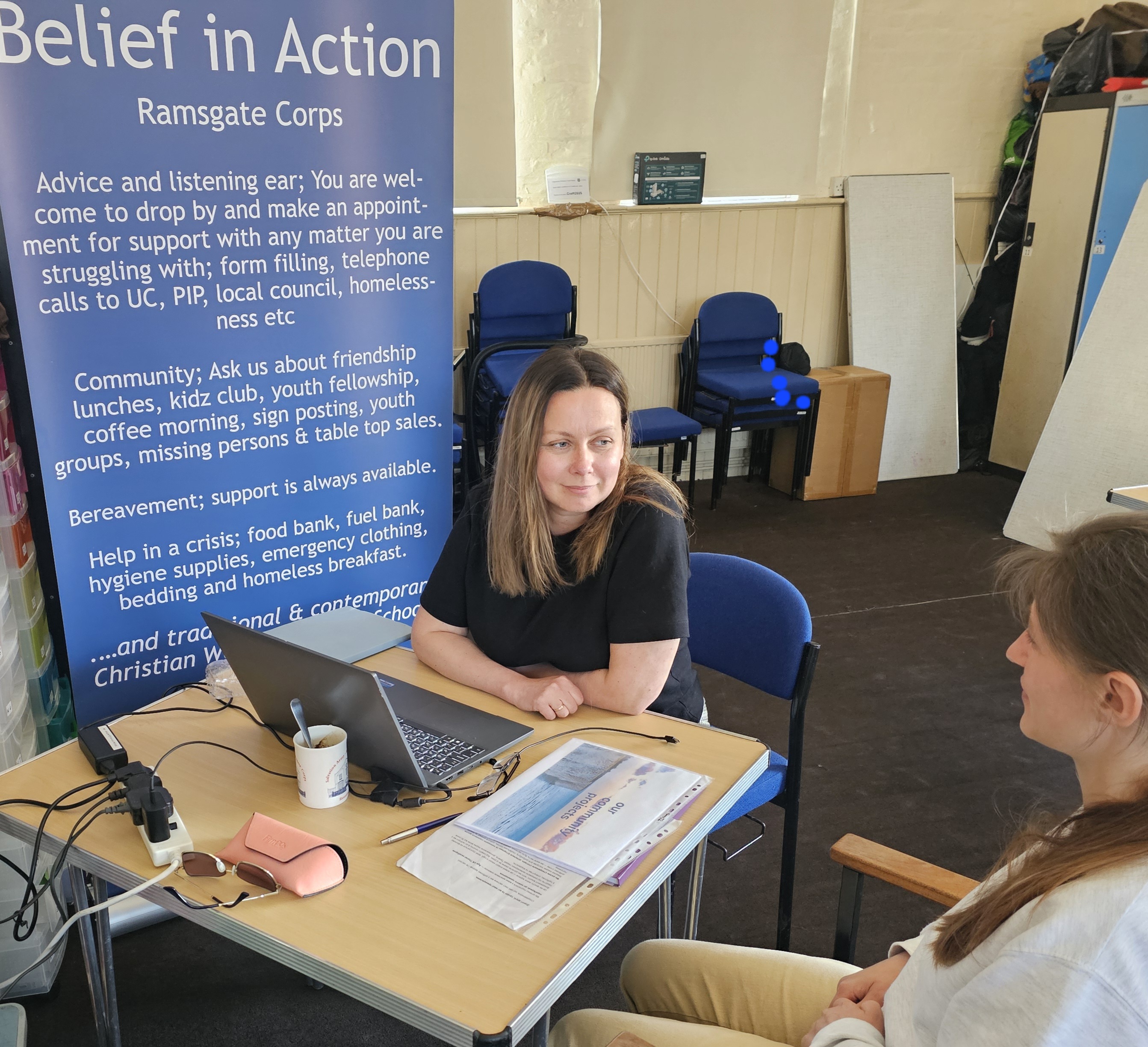 Two women discuss support at a desk with a laptop and information leaflets