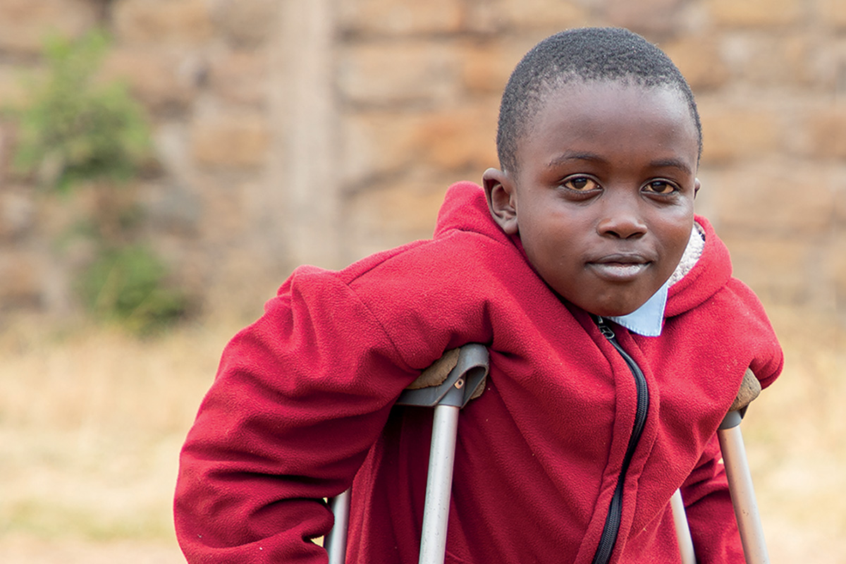 A young boy on crutches looks directly at the camera
