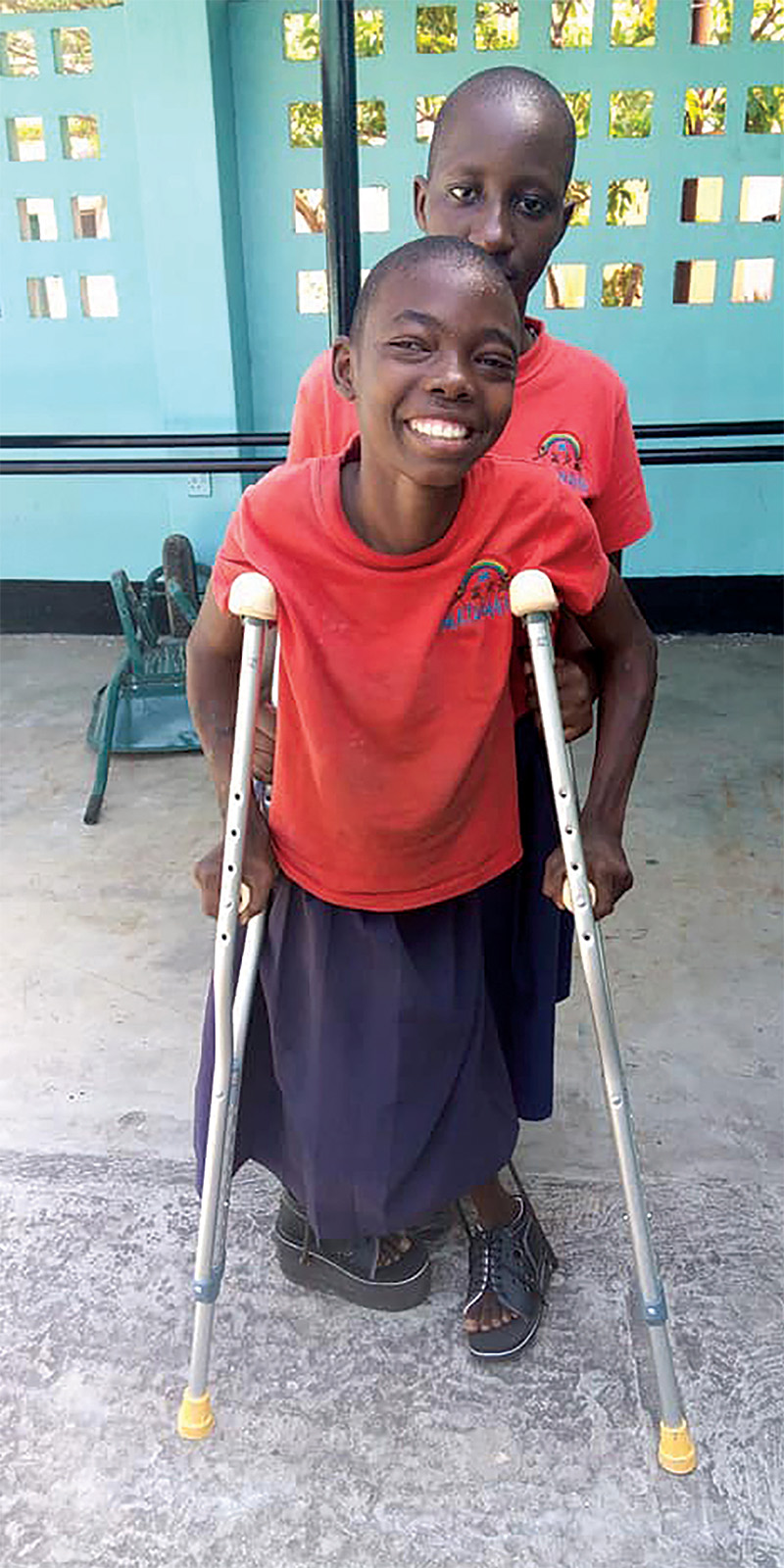 Two students, one using crutches, smile at the camera