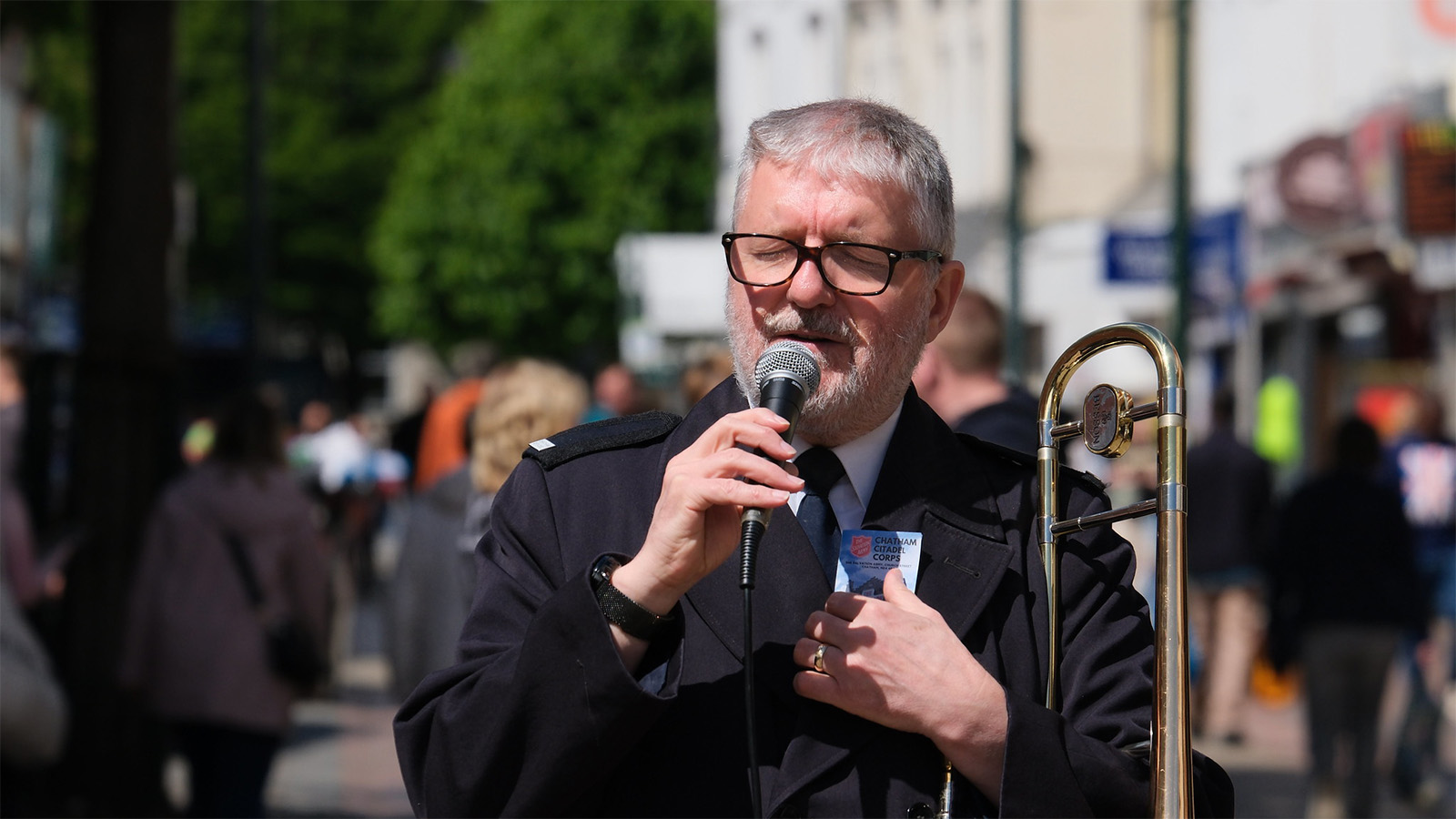 A Salvationist speaks into a microphone while holding a trombone