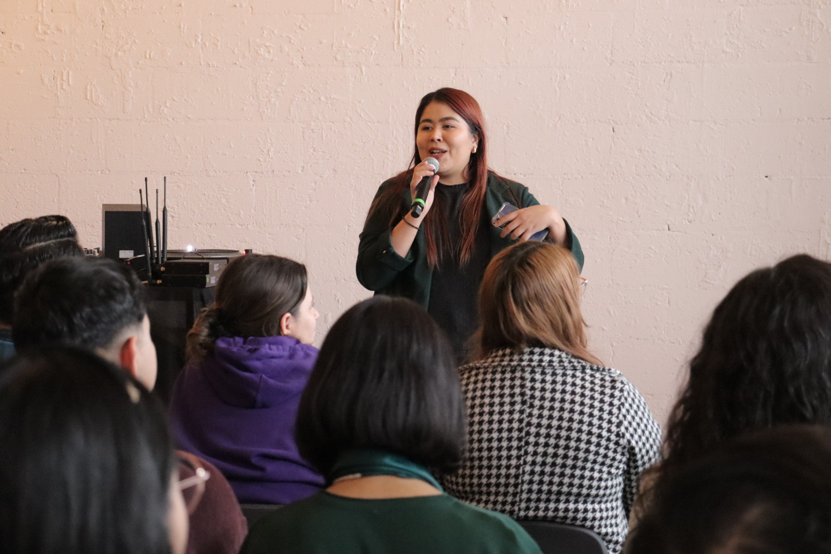 Fernanda stands at the front of the room with a microphone, addressing a crowd