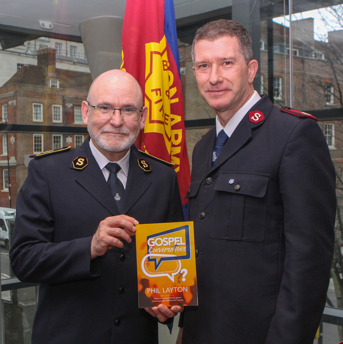 General Lyndon Buckingham holds a copy of Gospel Conversations, standing next to author Major Phil Layton