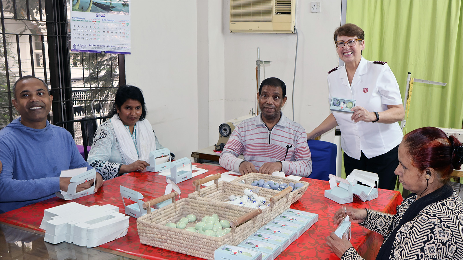 A group of artisans smile for the camera as they pack decorations into cardboard boxes. Commissioner Shelley Hill holds an example of the finished product.