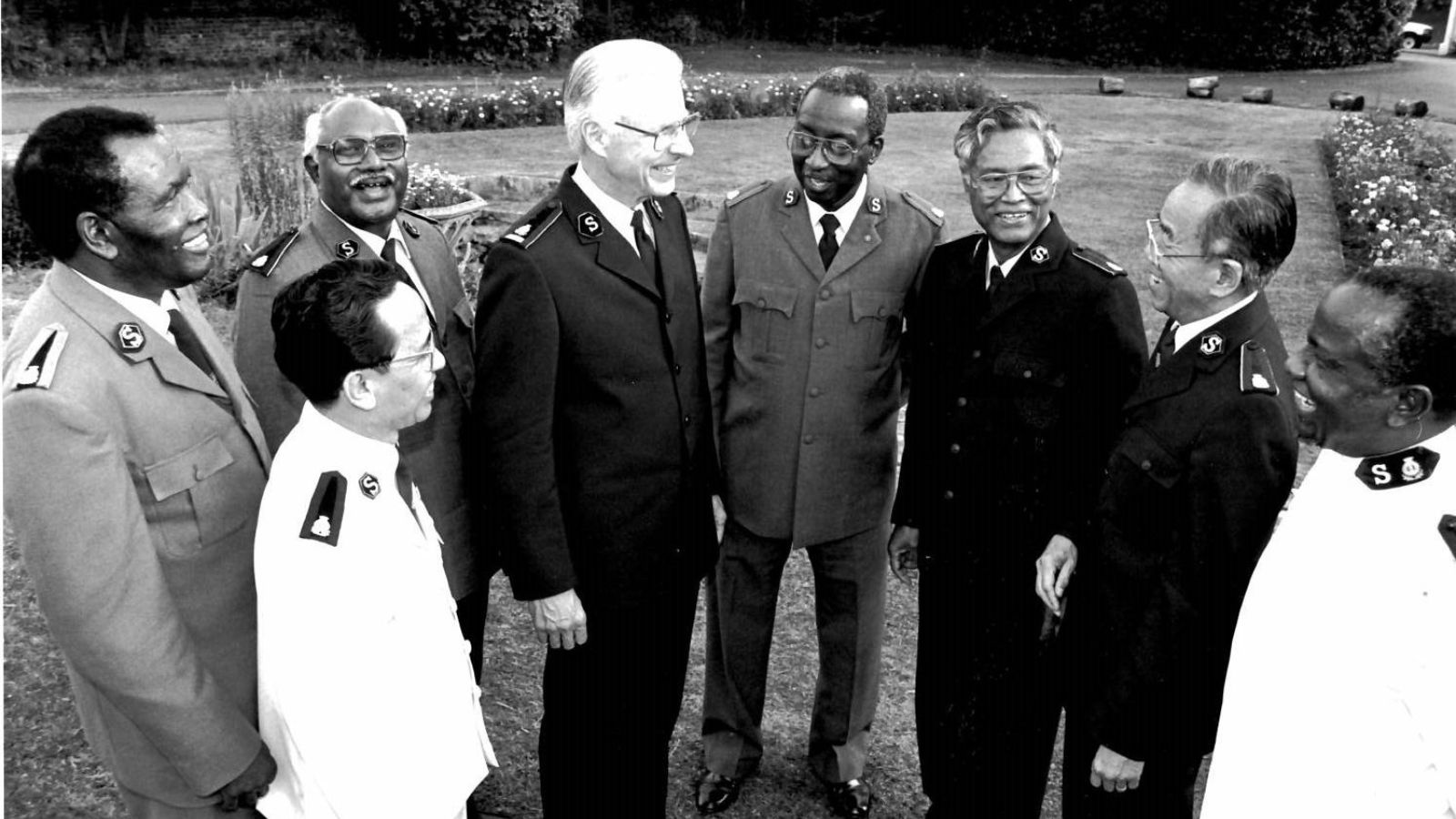 General Rader (Rtd) stands talking with seven other Salvation Army officers from around the world