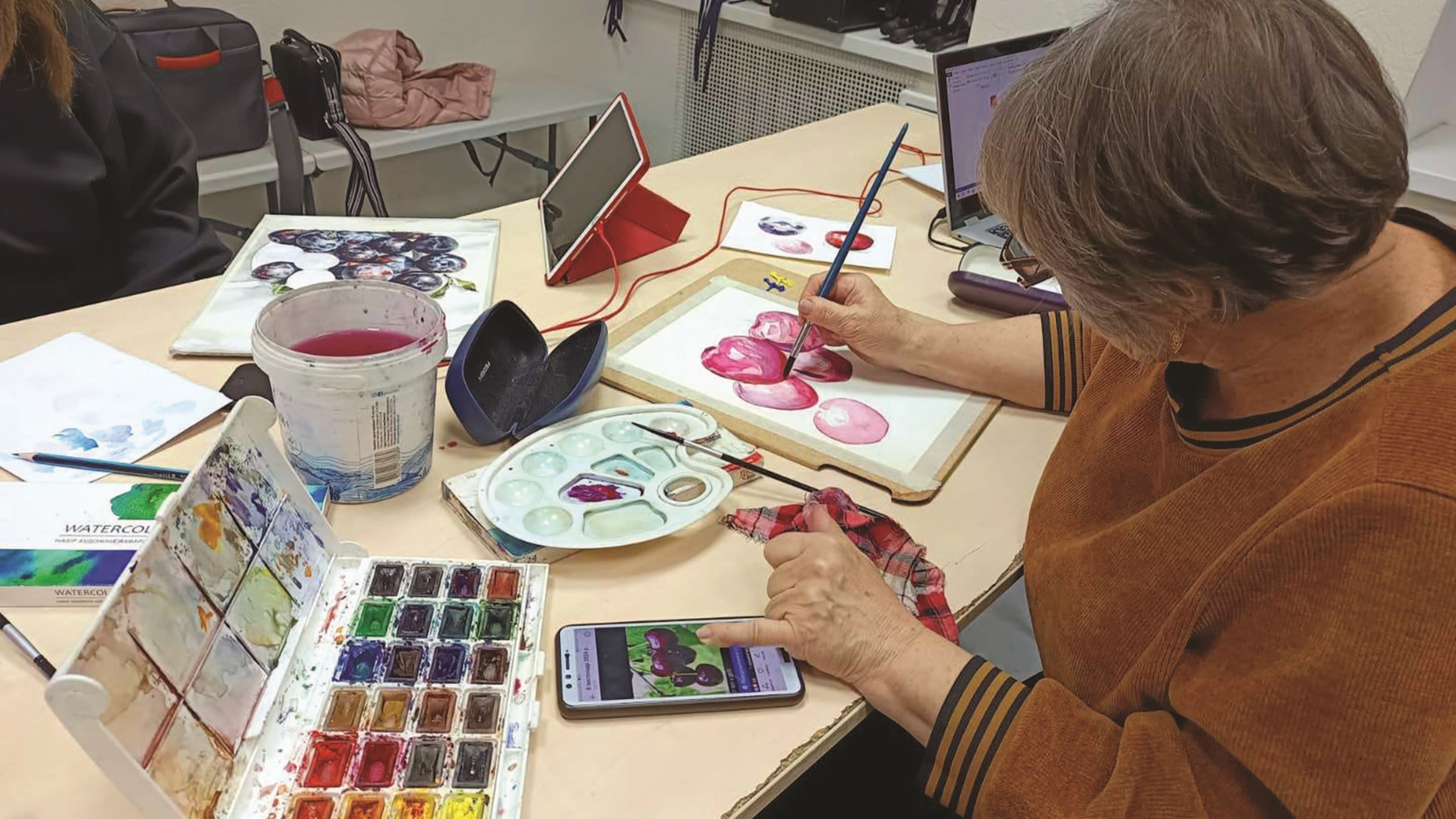 A woman paints a picture of fruit, using an image on a mobile phone as a reference