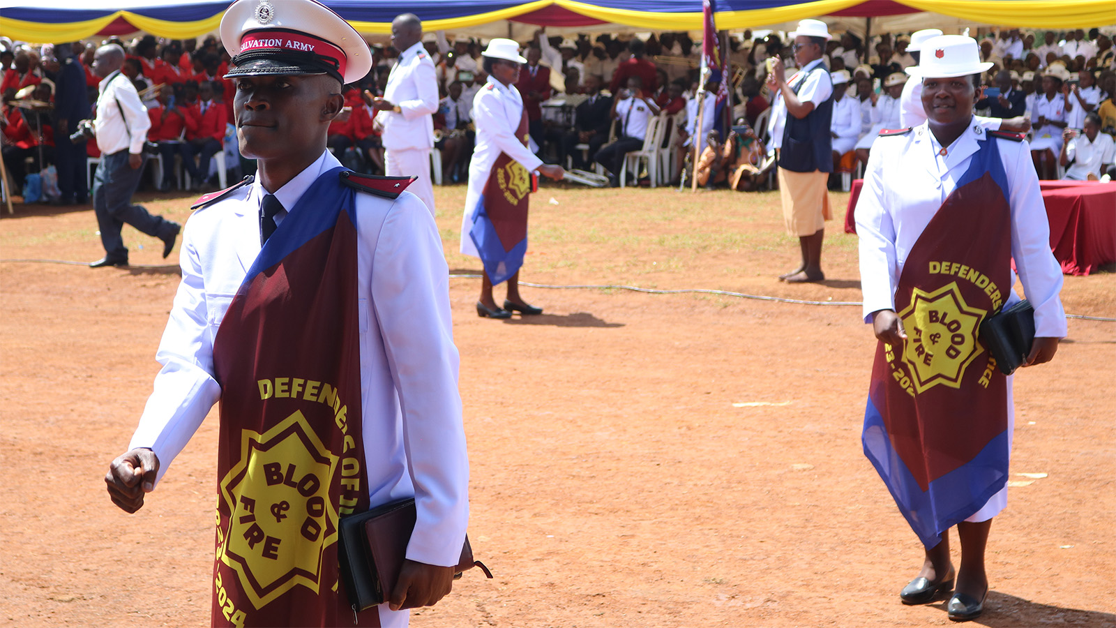 New lieutenants, dressed in white Salvation Army uniforms with their sessional flag, walk out in front of the congregation