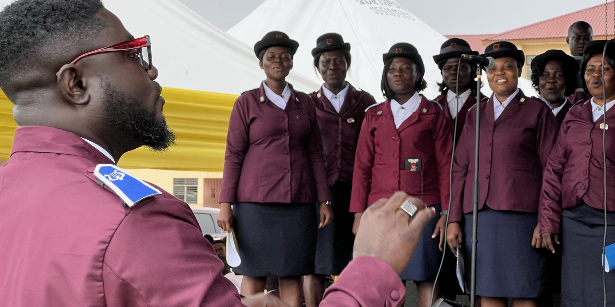 A man in red Salvation Army uniform conducts a choir