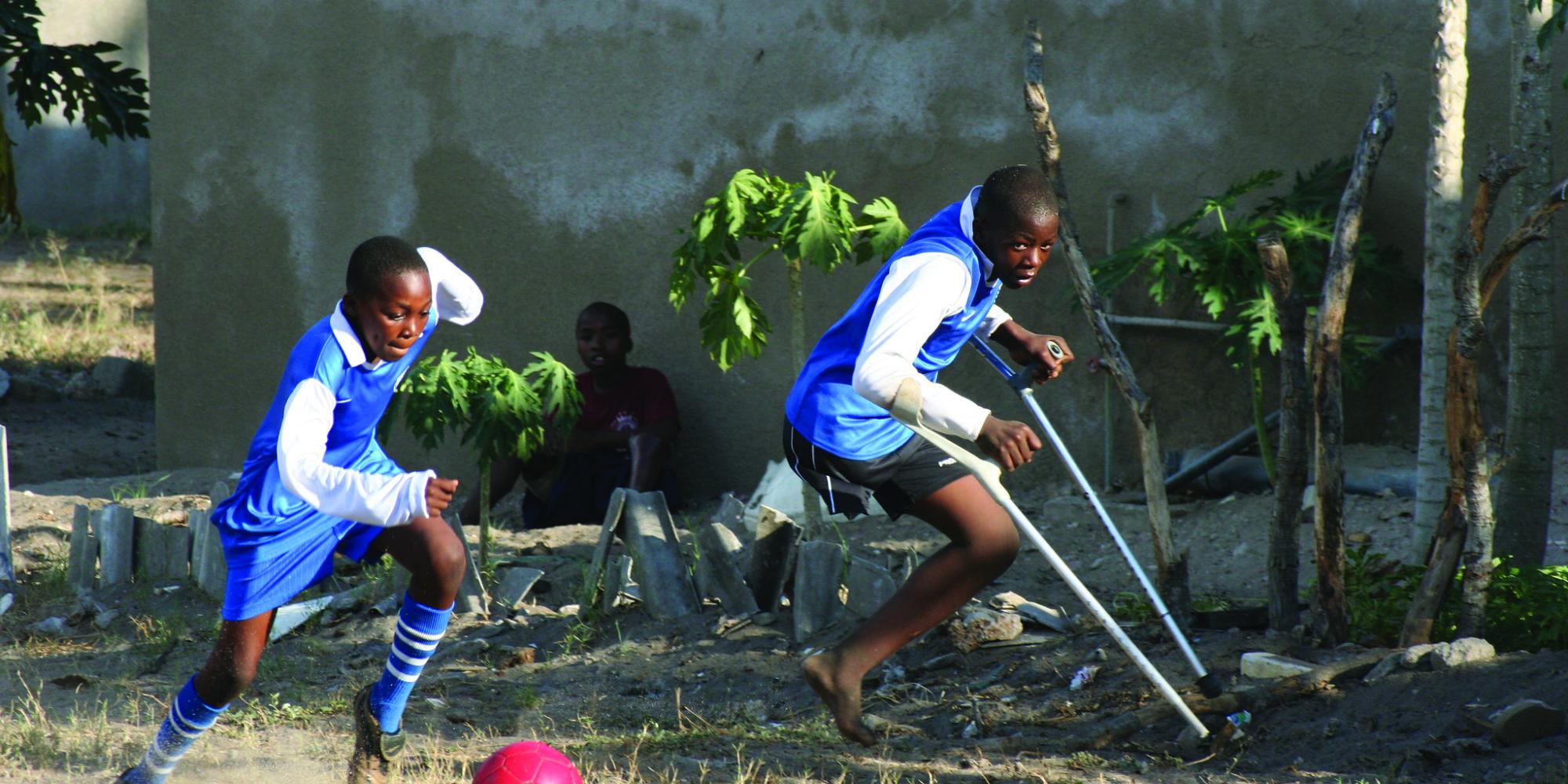 Two boys, one on crutches, play football