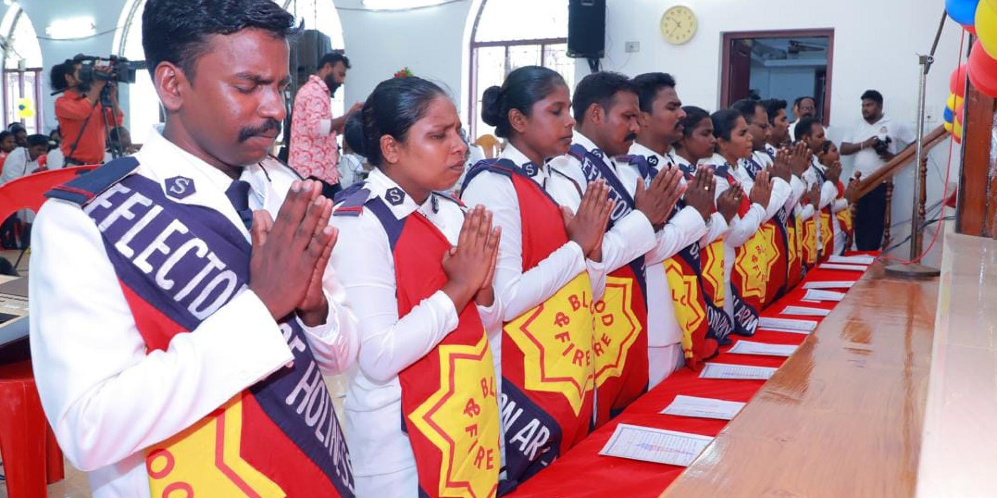 Men and women in Salvation Army uniform kneel in prayer