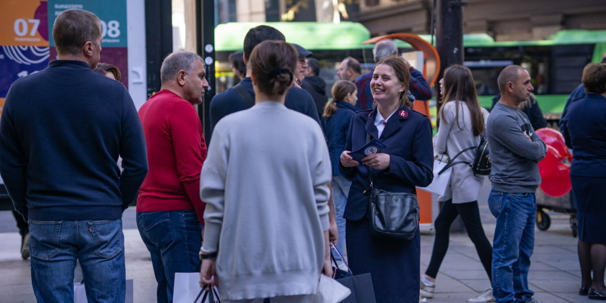 A woman in Salvation Army uniform speaks to people in a busy street