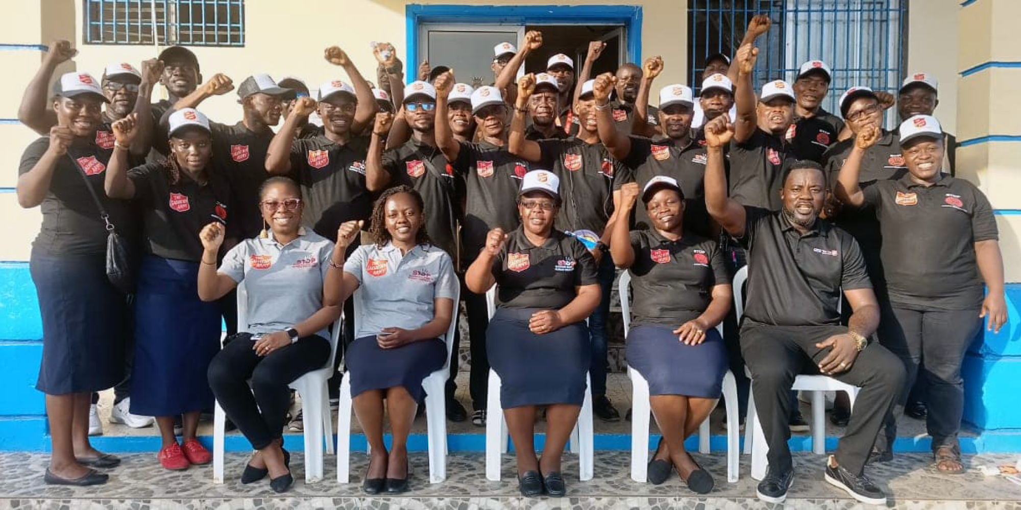 A group of people in Salvation Army polo shirts raise their hands in victory