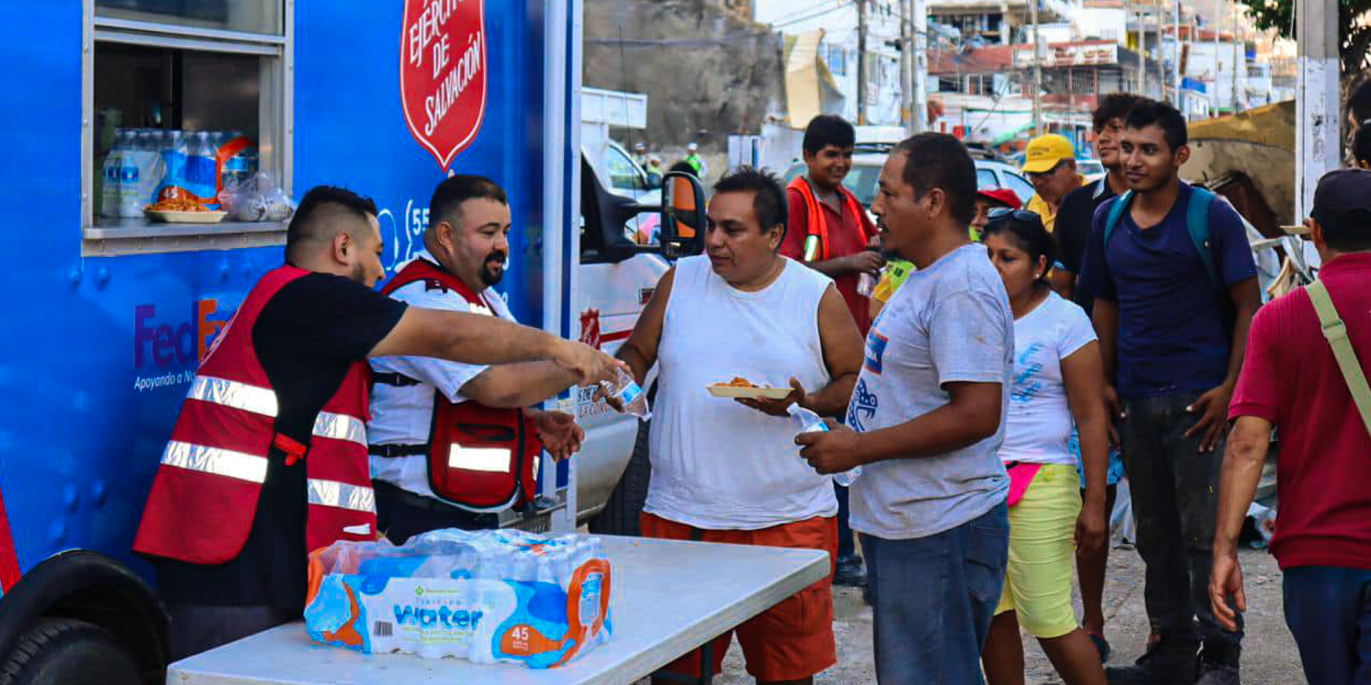 Men hand out water in front of a Salvation Army emergency vehicle