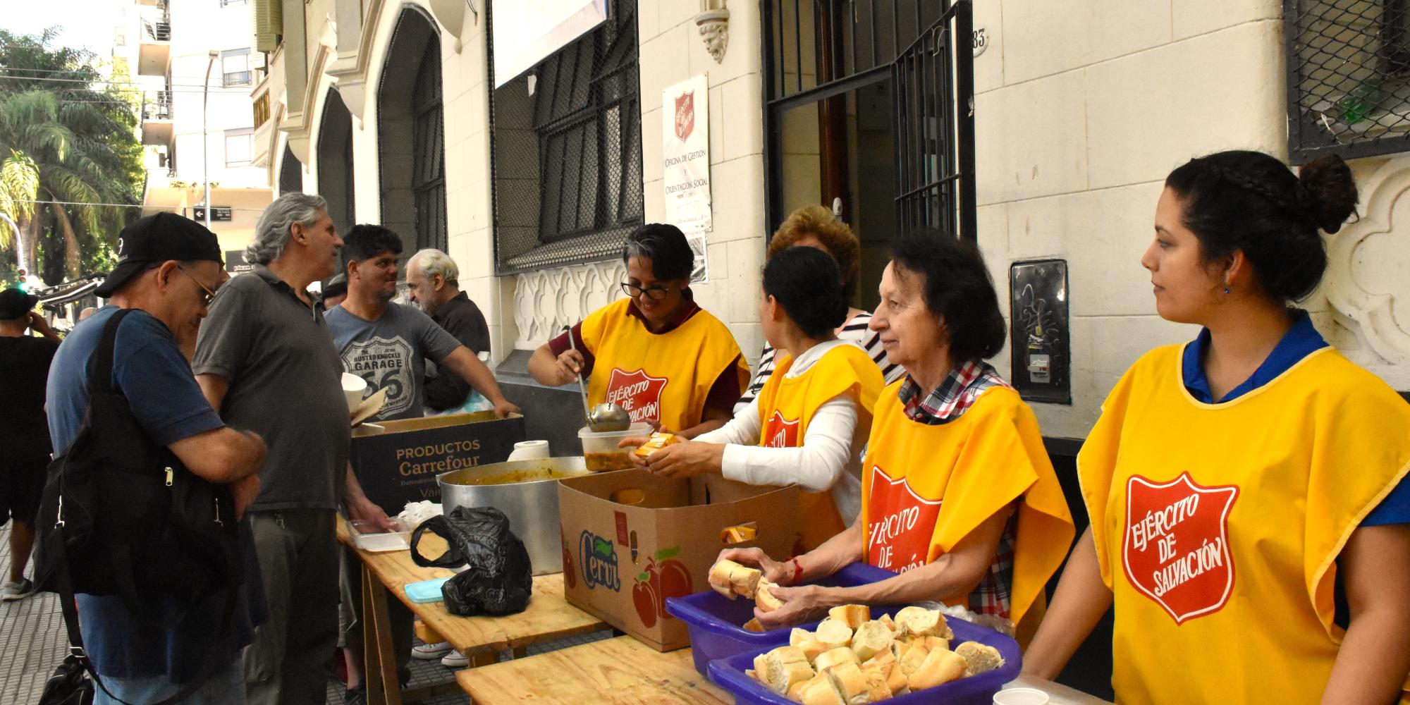 People in Salvation Army tabards serve soup from tables in the street
