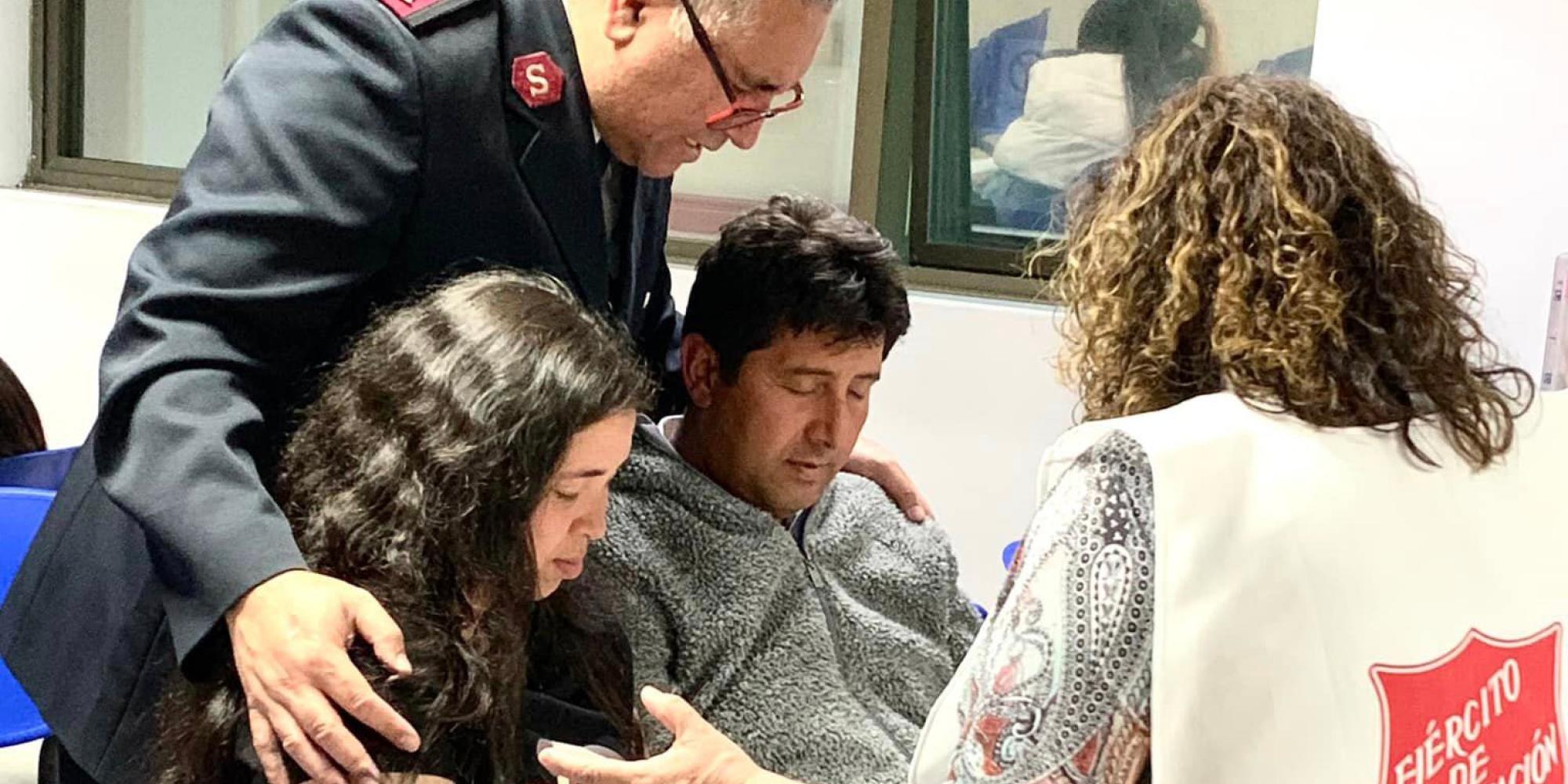 Two people in Salvation Army clothes pray with a couple