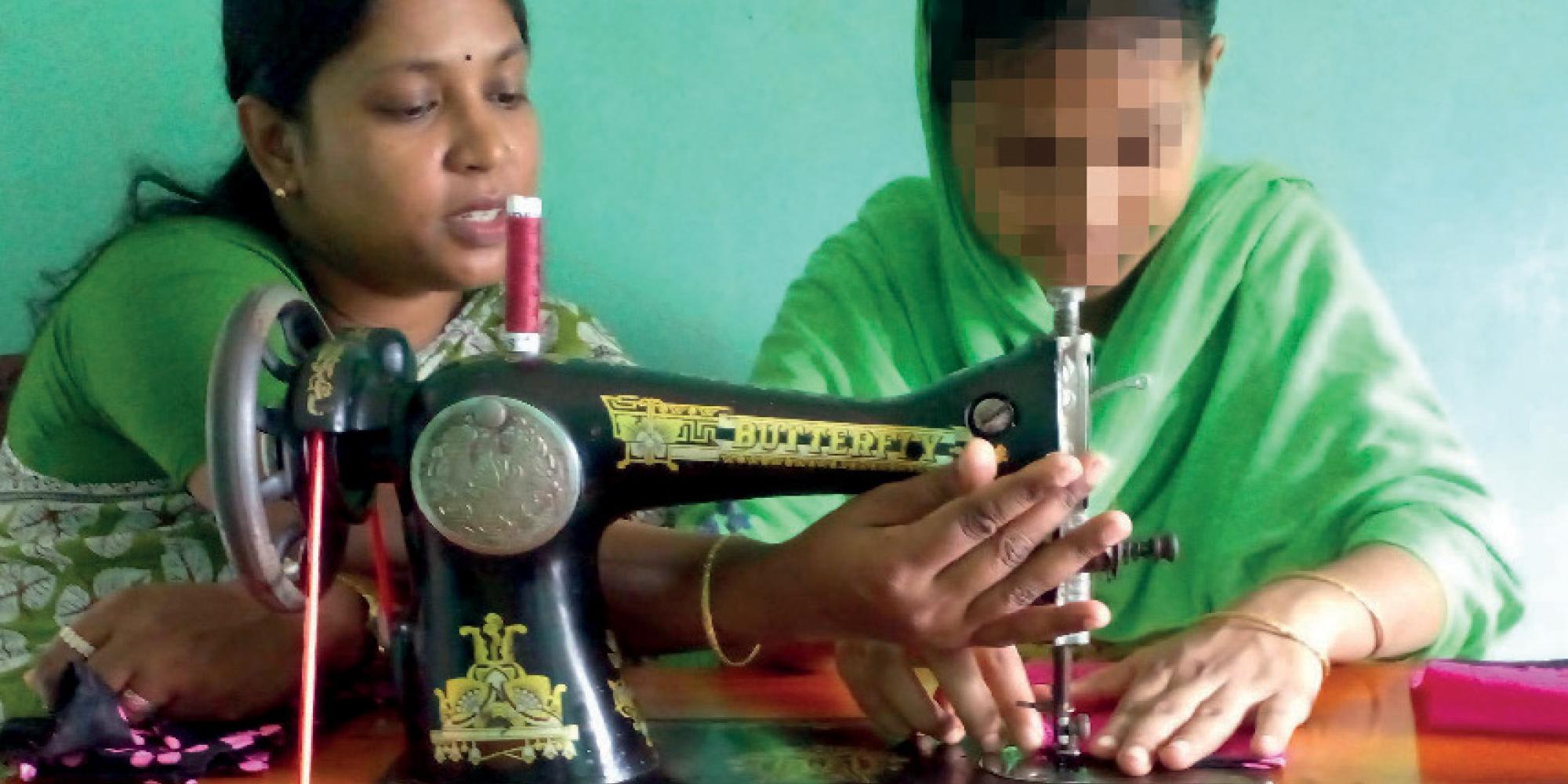 Two women sitting at a sewing machine, one with her face blurred