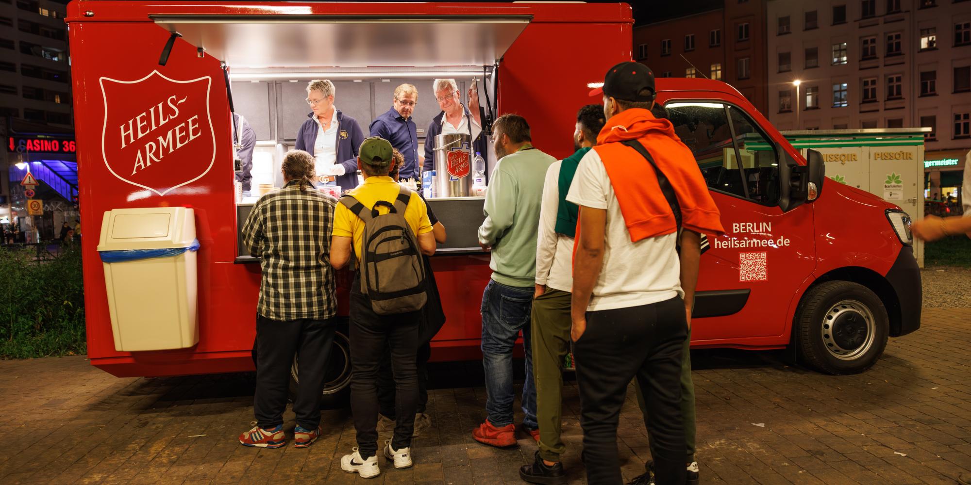 People queue for food in front of a red Salvation Army van