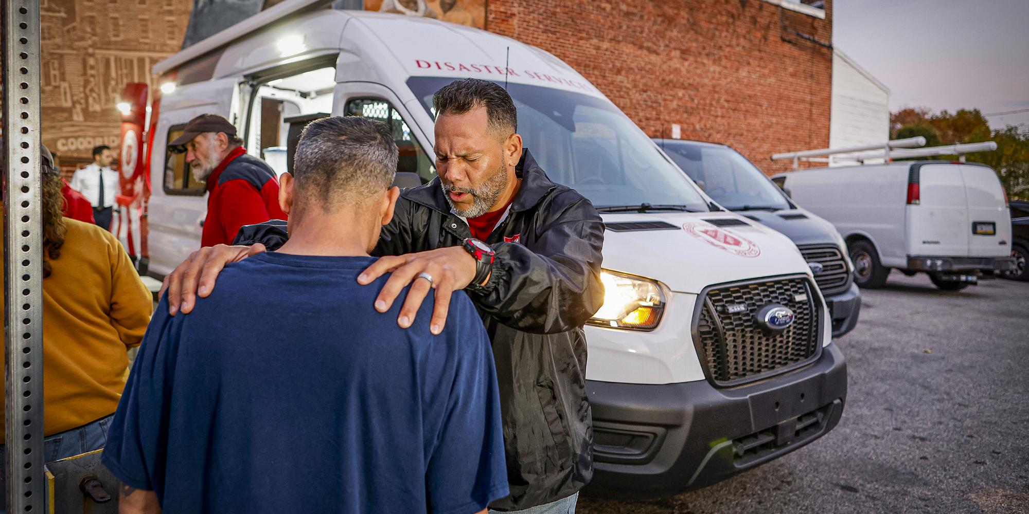 Two men pray in front of a Salvation Army emergency vehicle