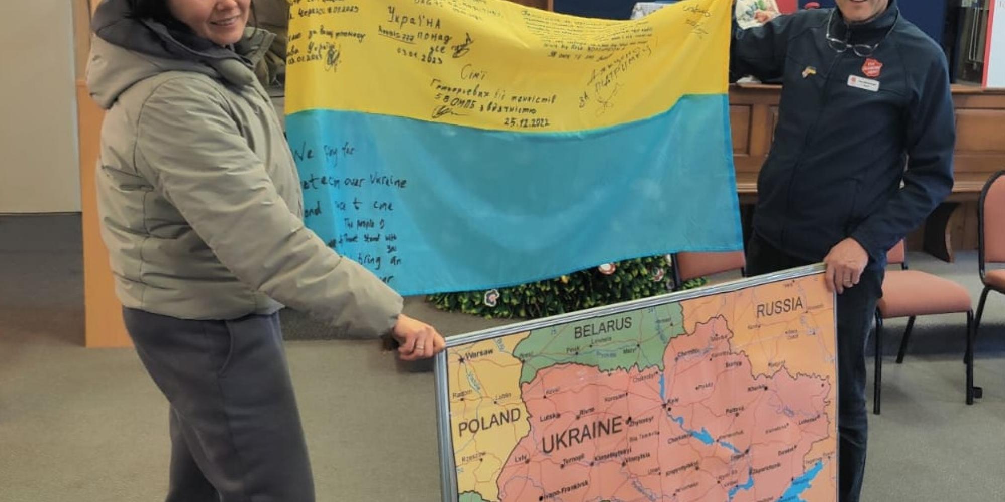 A woman and a man in Salvation Army uniform hold a Ukrainian flag and a map of the region