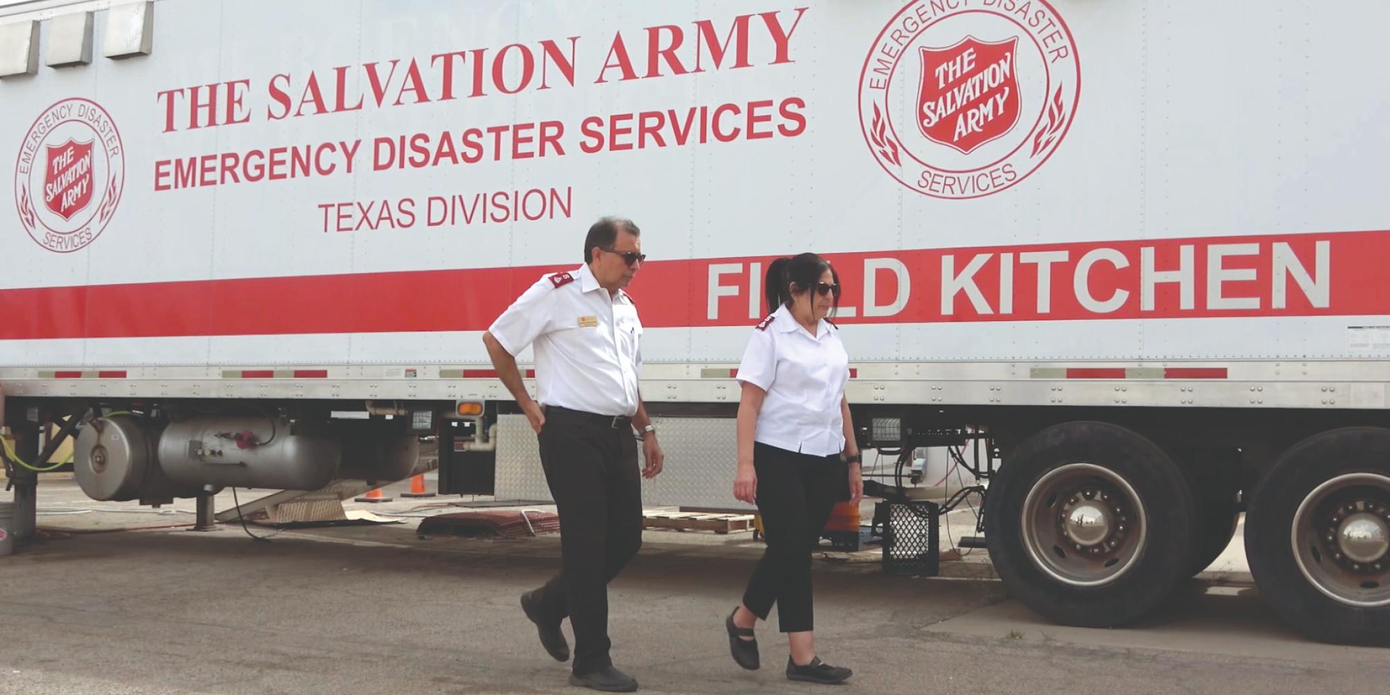 Two people in Salvation Army uniform walk past a field kitchen