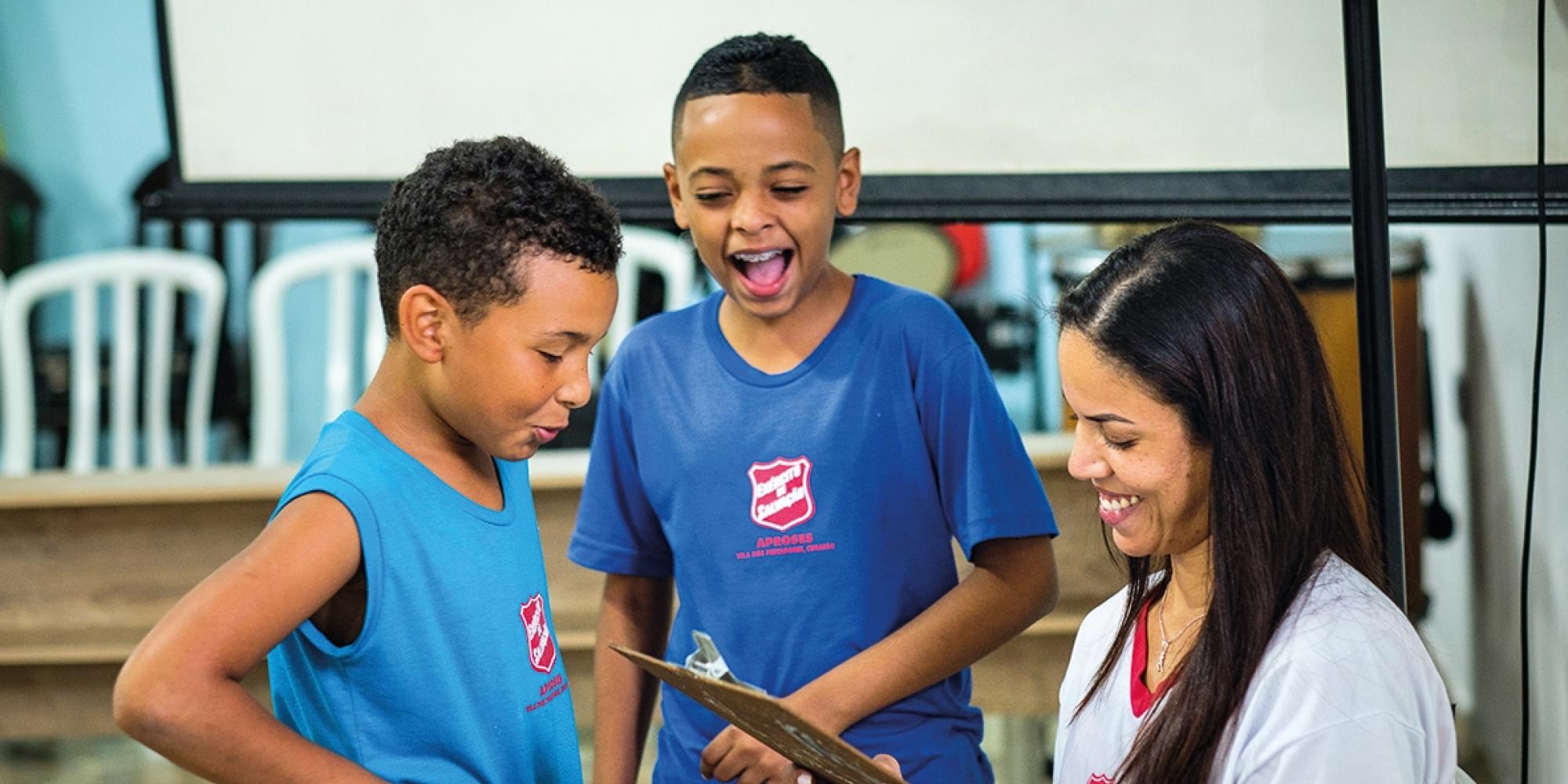 Children in Salvation Army t-shirts laugh together as a volunteer checks a clipboard