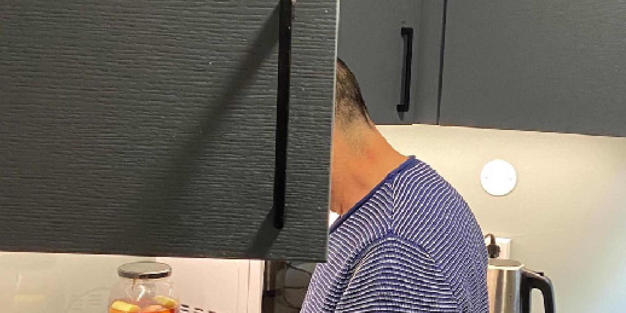 A man washes dishes, his face hidden by an open cupboard door