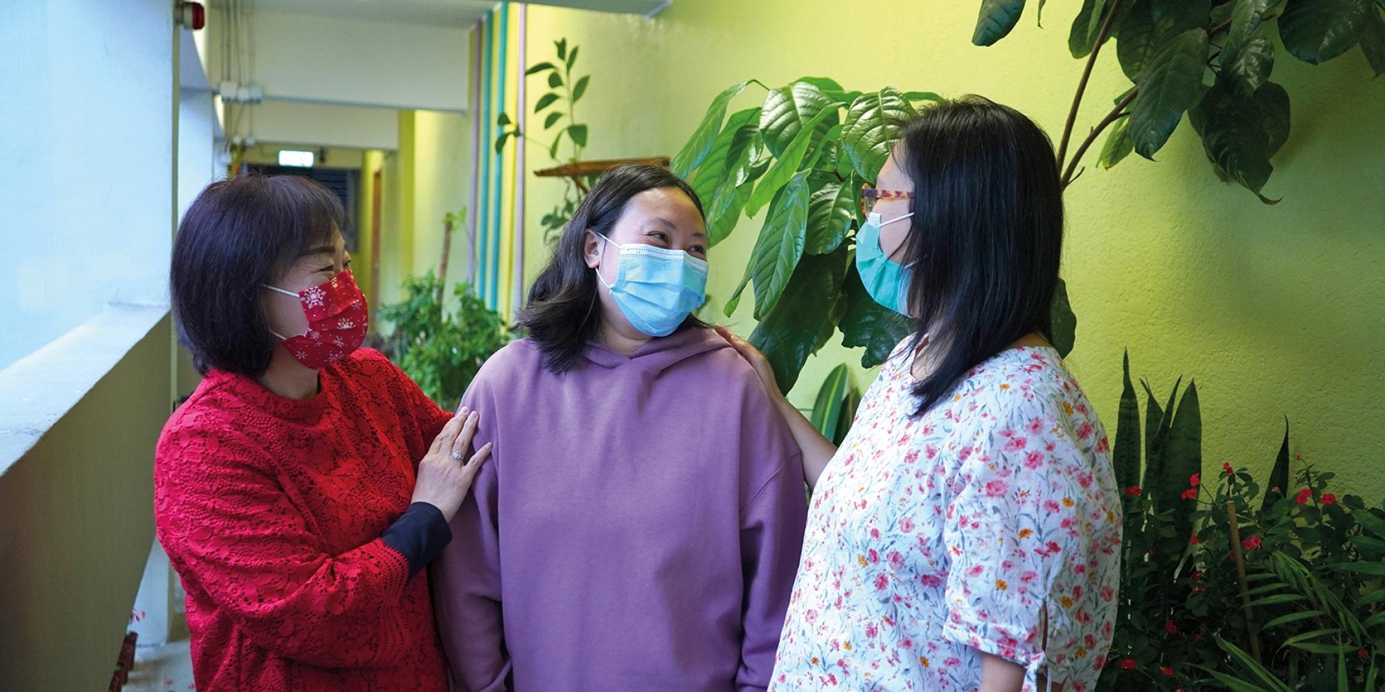 Three women, wearing facemasks, chat together