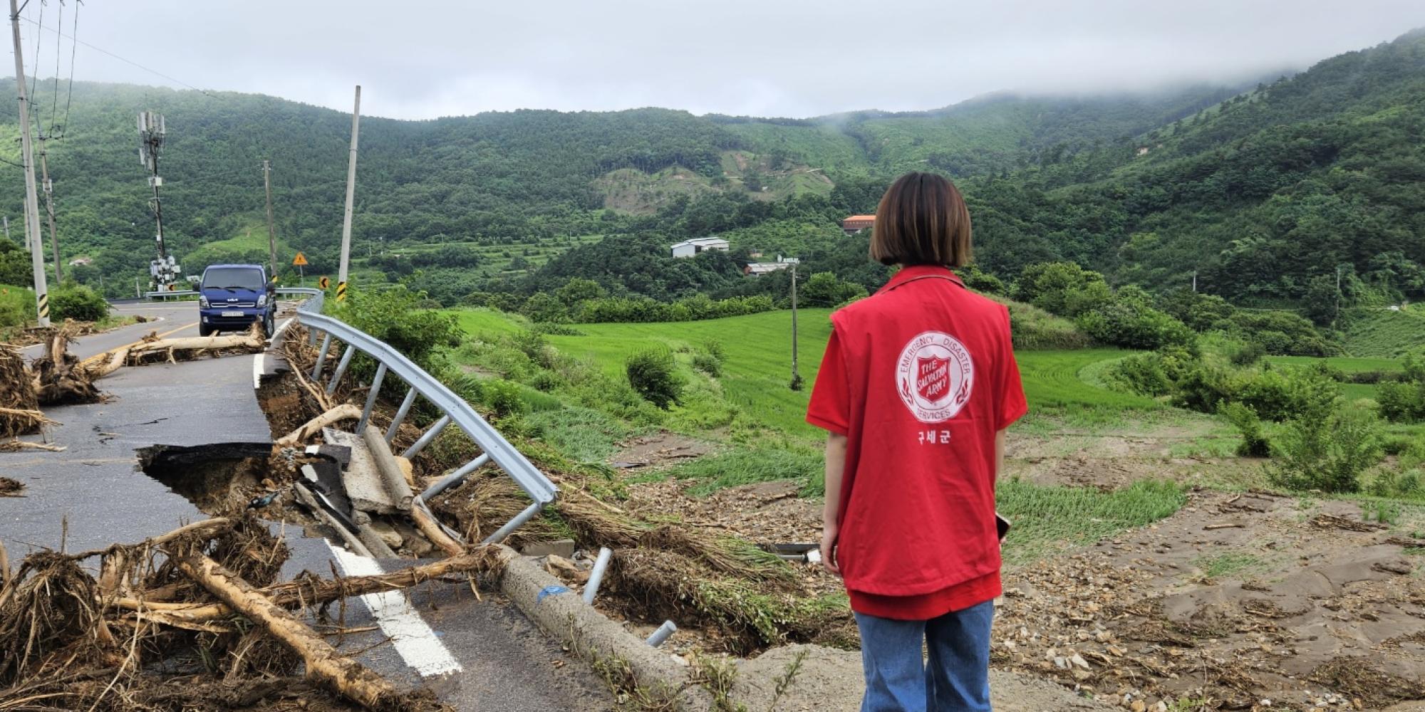 A person in a Salvation Army t-shirt looks out at a flood-damaged road