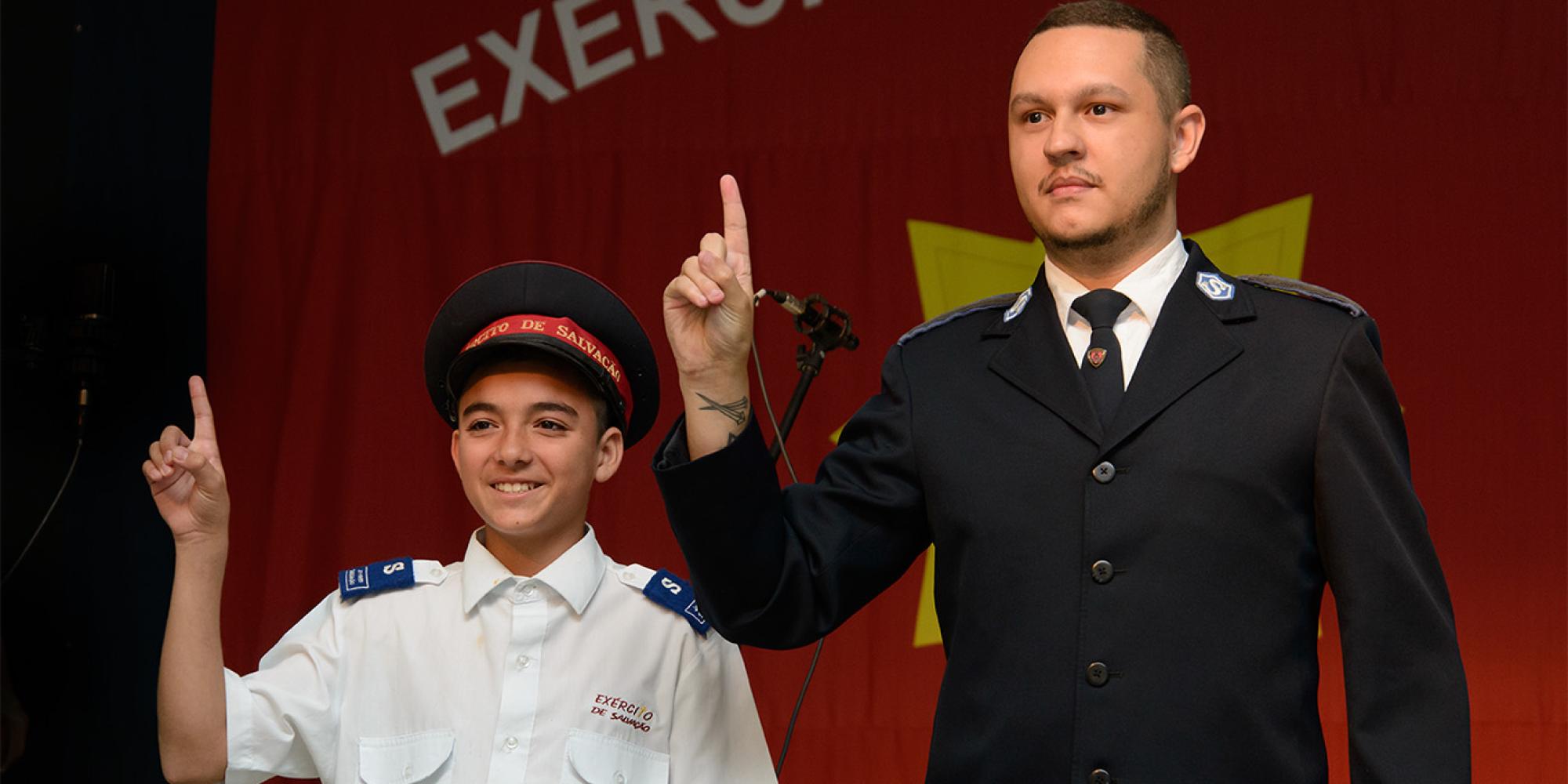 A young junior soldier, wearing a cap, and a senior soldier give the Salvation Army salute