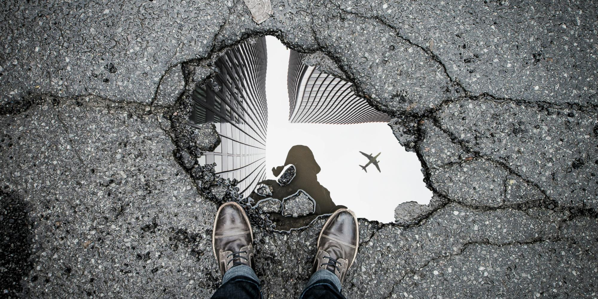 A man looks down at his reflection in a puddle