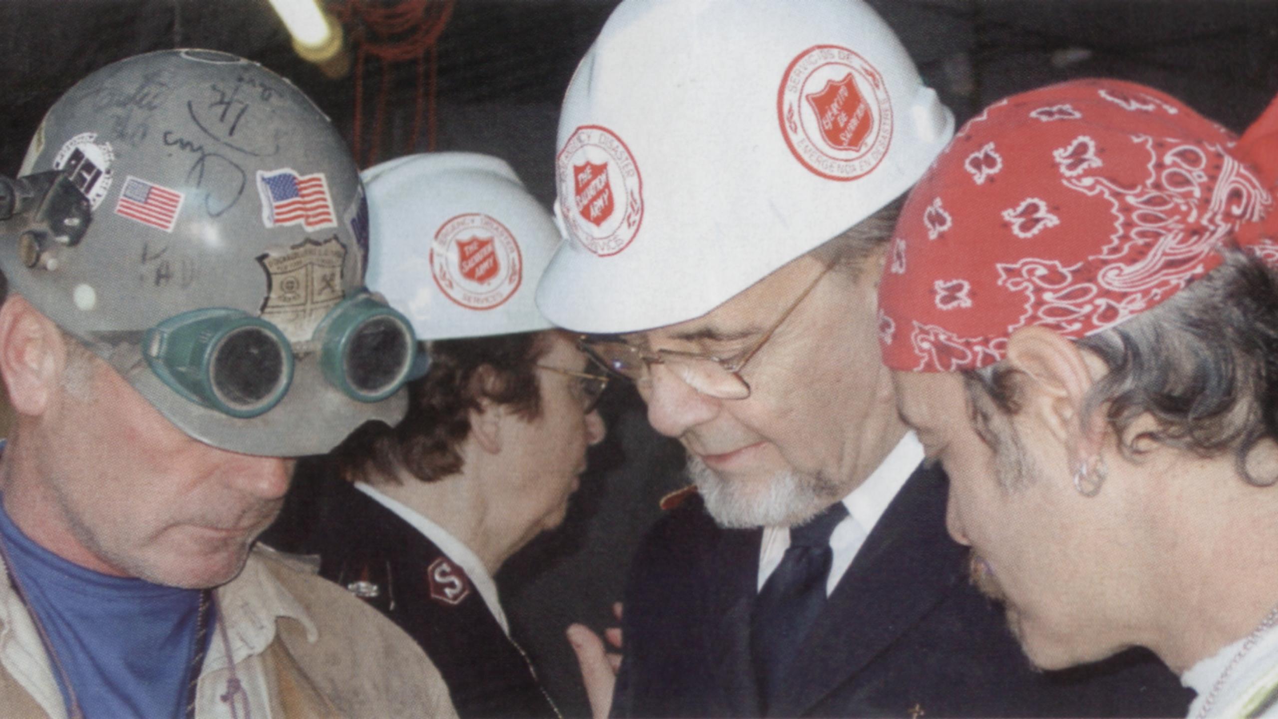 General John Gowans, head bowed in prayer, wears a Salvation Army hard hat