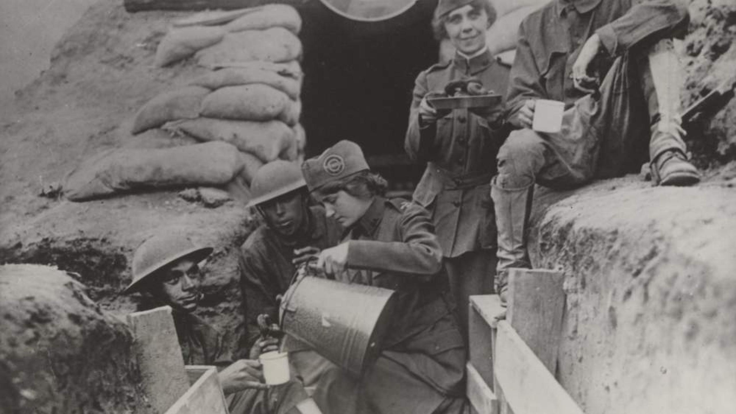 Two women in Salvation Army uniform serve coffee and doughnuts to soldiers in a trench