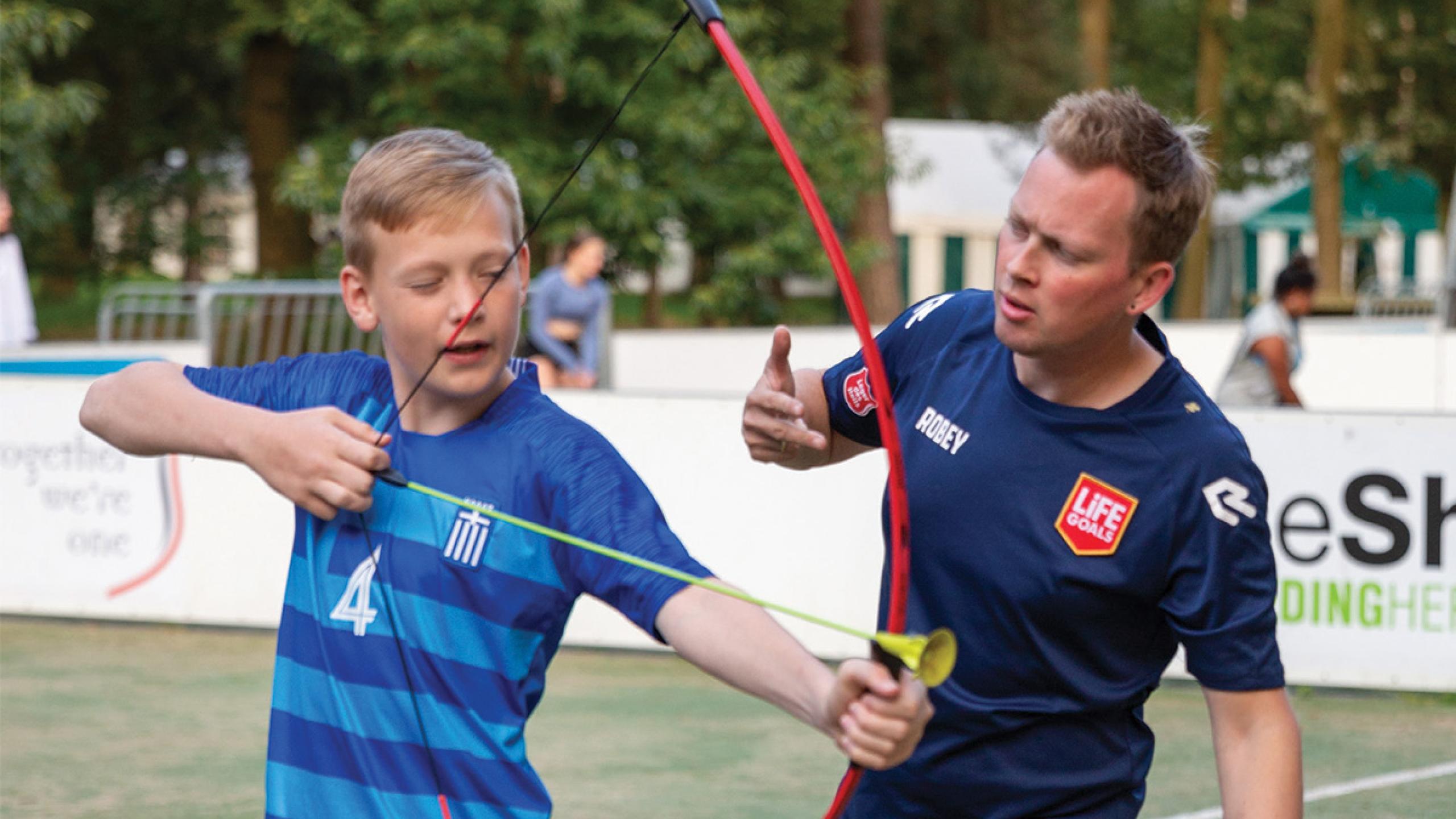 A man teaches a boy to shoot a bow and arrow