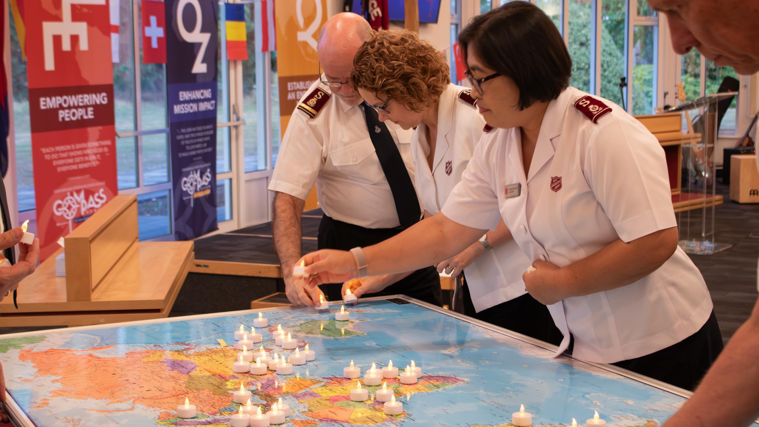 Salvation Army officers place electric candles on a map of the world