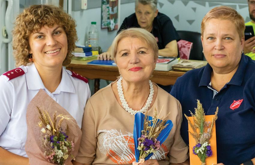 Three women, two wearing Salvation Army clothing, hold flower bouquets