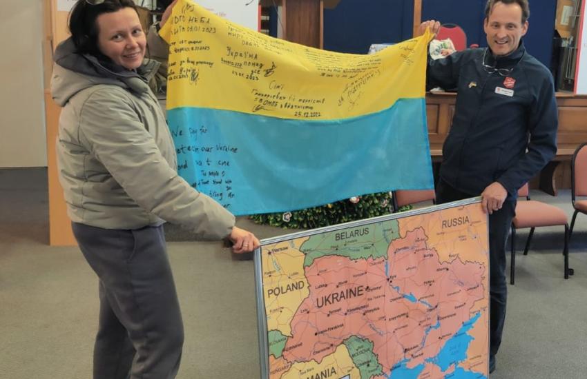 A woman and a man in Salvation Army uniform hold a Ukrainian flag and a map of the region