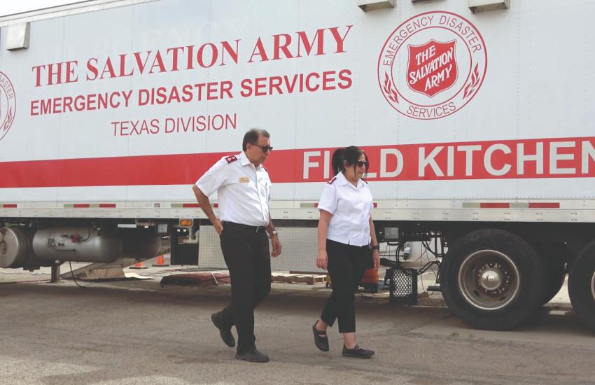 Two people in Salvation Army uniform walk past a field kitchen