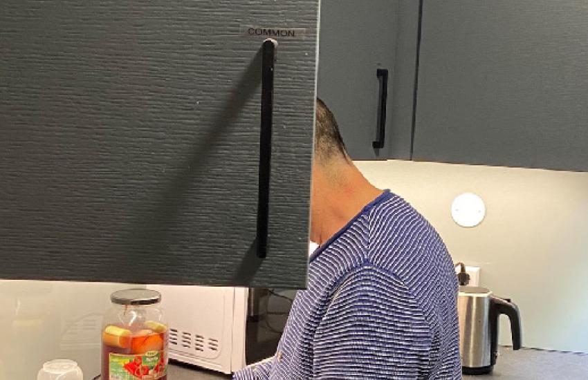 A man washes dishes, his face hidden by an open cupboard door