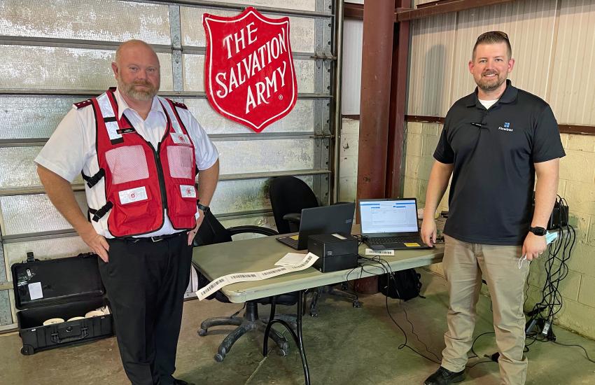 Two men stand in front of a Salvation Army shield