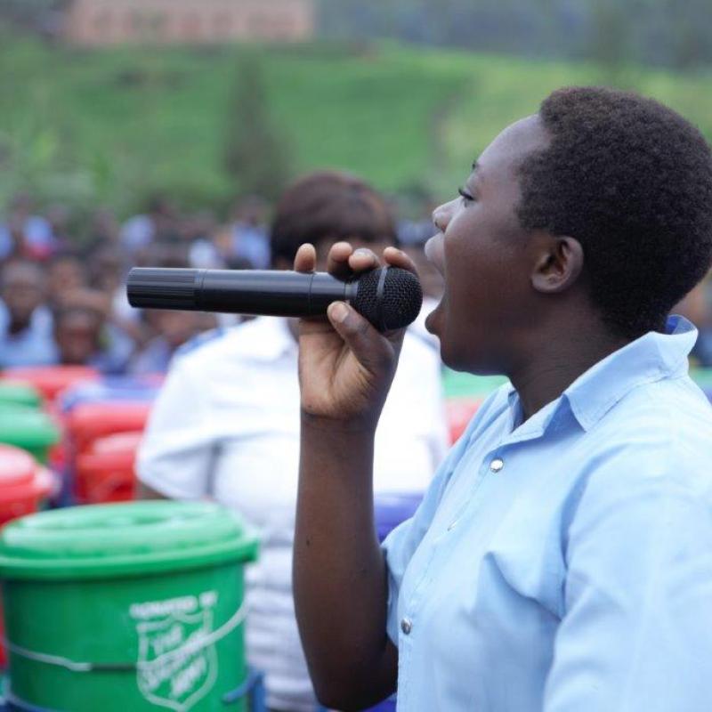 A woman speaks into a microphone in front of a large crowd and a collection of Salvation Army branded buckets