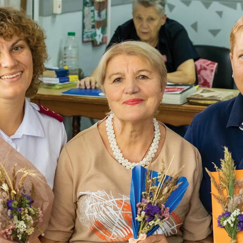 Three women, two wearing Salvation Army clothing, hold flower bouquets