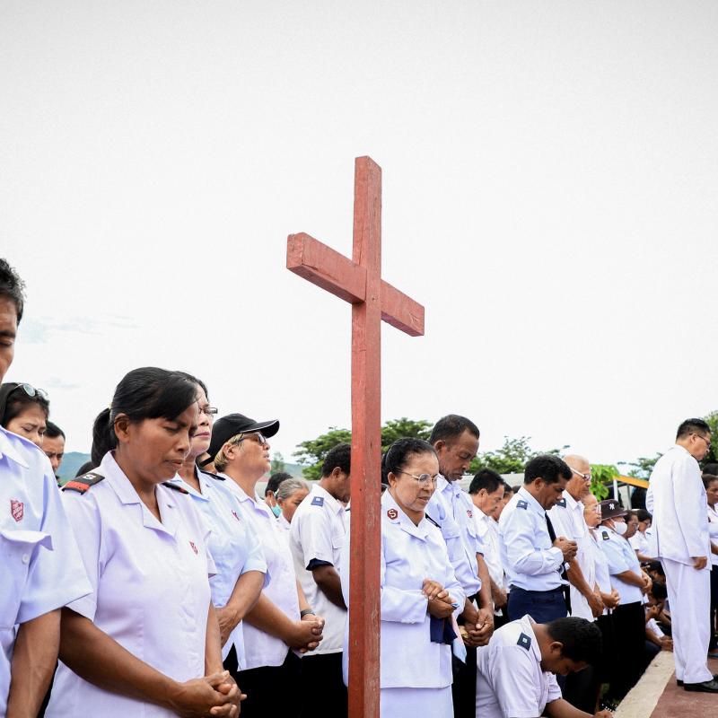 A group of Indonesian Salvationists bow their heads in prayer, gathered around a cross