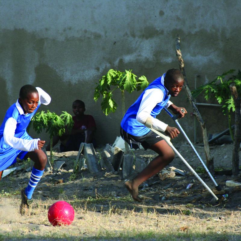 Two boys, one on crutches, play football