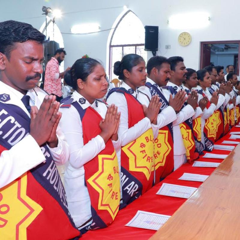 Men and women in Salvation Army uniform kneel in prayer
