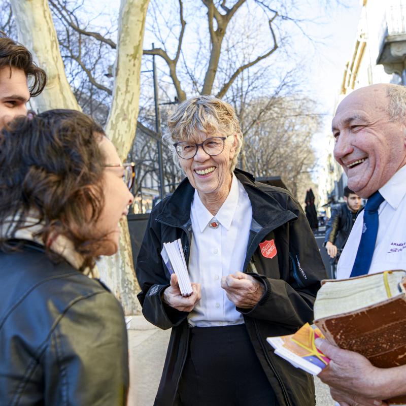 A woman and a man in Salvation Army uniform speak to people on the street