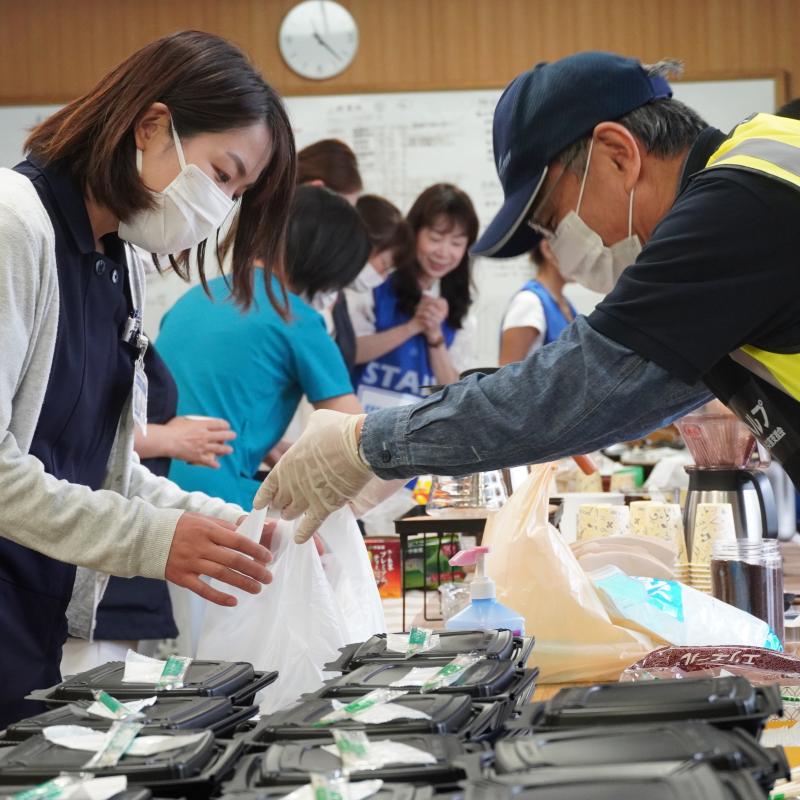 A man in a Salvation Army hi-vis jacket hands a woman a bag