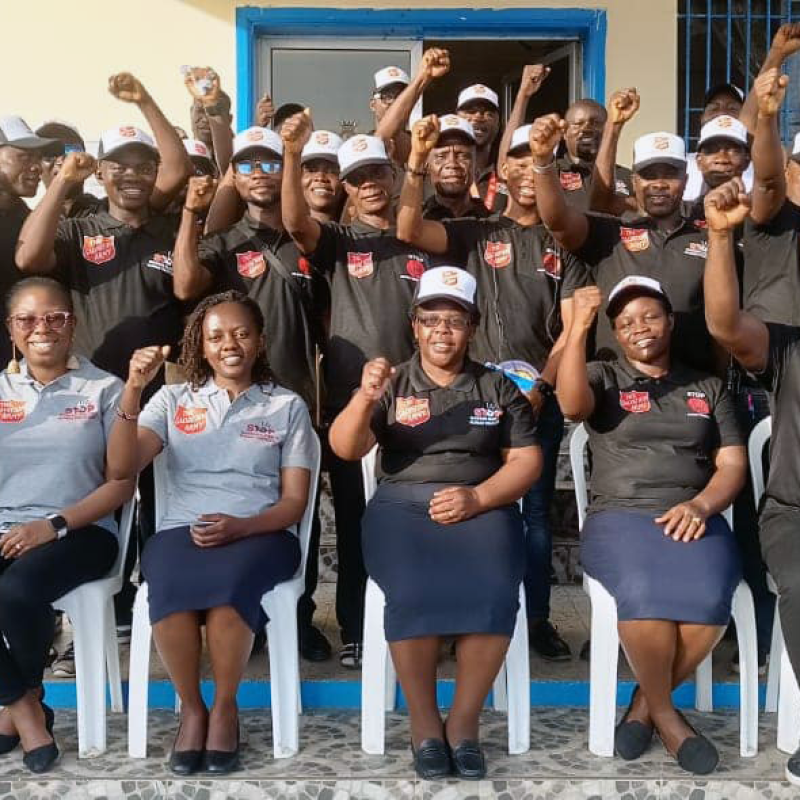 A group of people in Salvation Army polo shirts raise their hands in victory