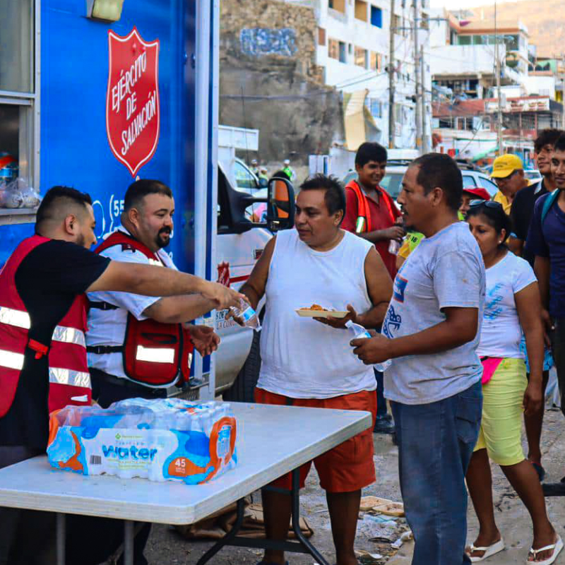 Men hand out water in front of a Salvation Army emergency vehicle